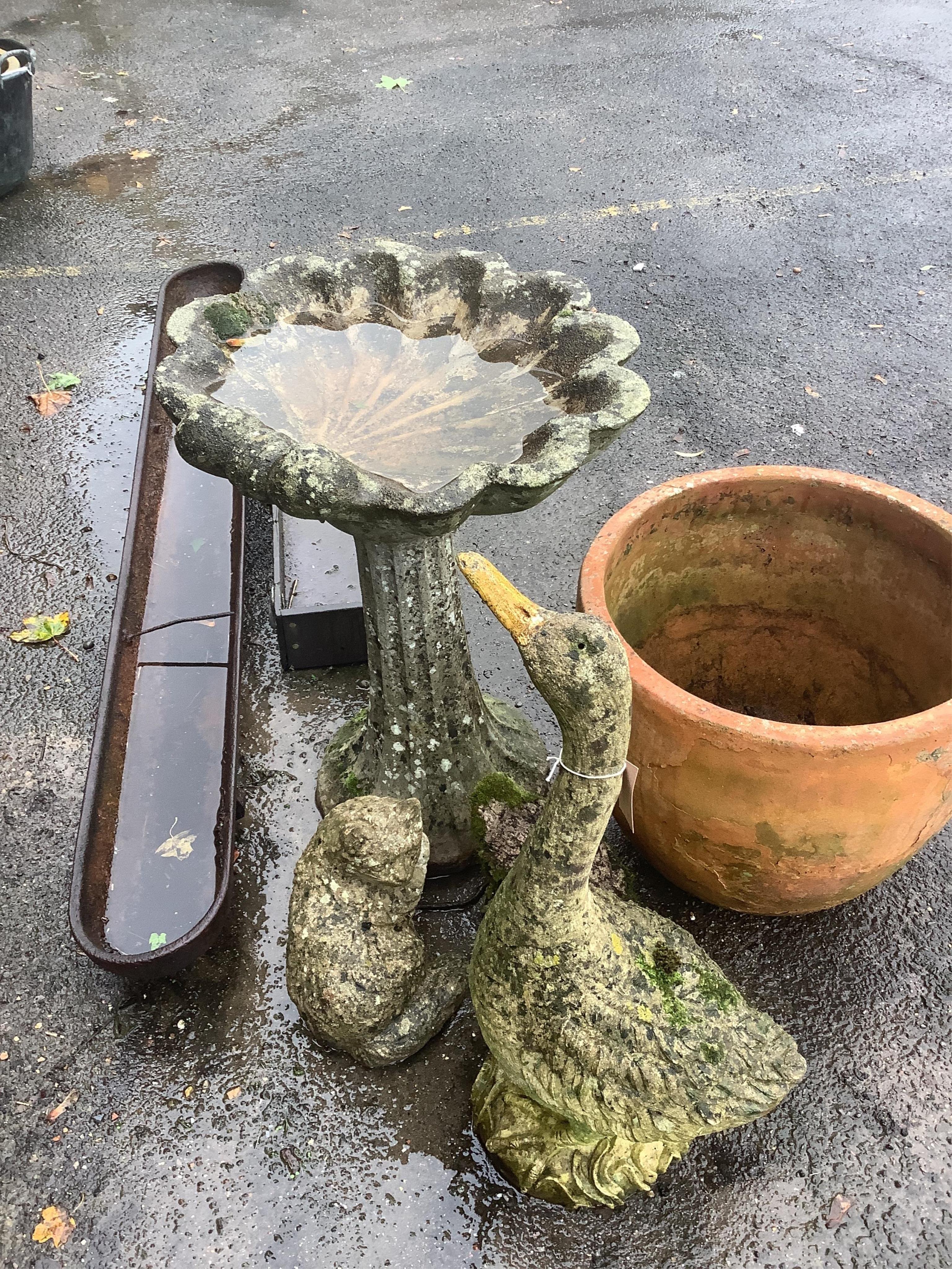 A reconstituted stone scallop shell bird bath, height 71cm, three reconstituted stone garden ornaments, a terracotta planter and two feeding troughs. Condition - fair